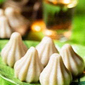 modak or modakam placed on a green leaf shaped platter on green colored board.