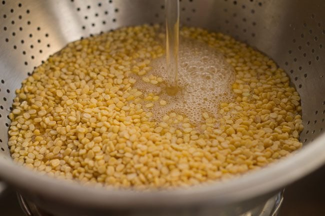 rinsing yellow moong lentils with water in colander