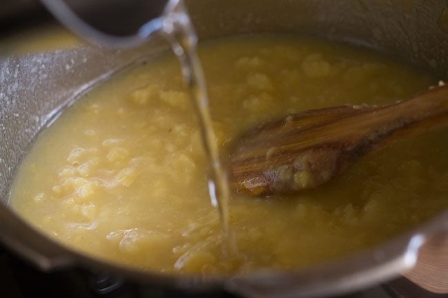 water being added to mashed yellow moong dal