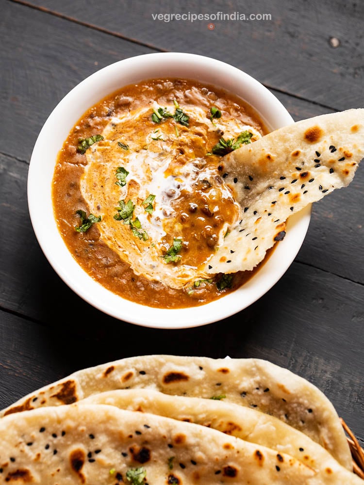 naan bread dipped in dal makhani in a white bowl