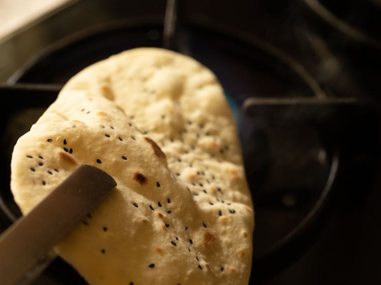 cooking naan on direct flame using tongs