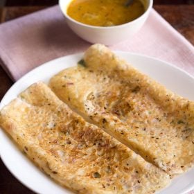 onion dosa served on a white plate with a side of sambar.