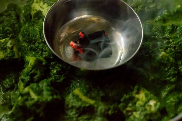 red hot coal with oil placed in steel bowl on top of palak paneer