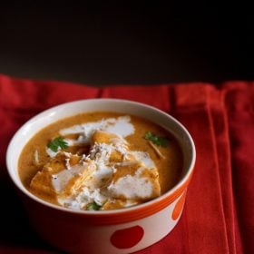 paneer makhanwala topped with cream, grated paneer, coriander leaves in an orange dotted bowl on a red cotton napkin.
