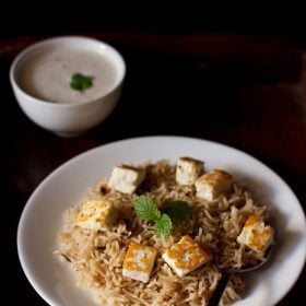 paneer pulao served on a white plate with a side of raita.