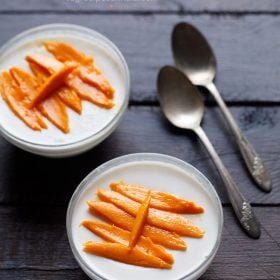 two bowls of panna topped with mango slices with a side of dessert spoons.