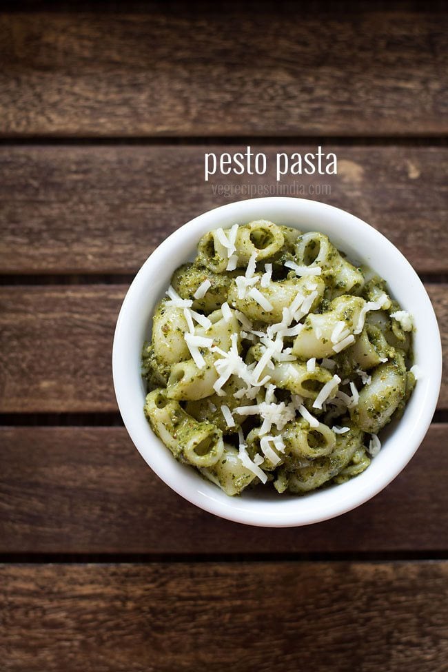 pesto pasta served in a white bowl topped with some grated parmesan on a dark brown wooden tray