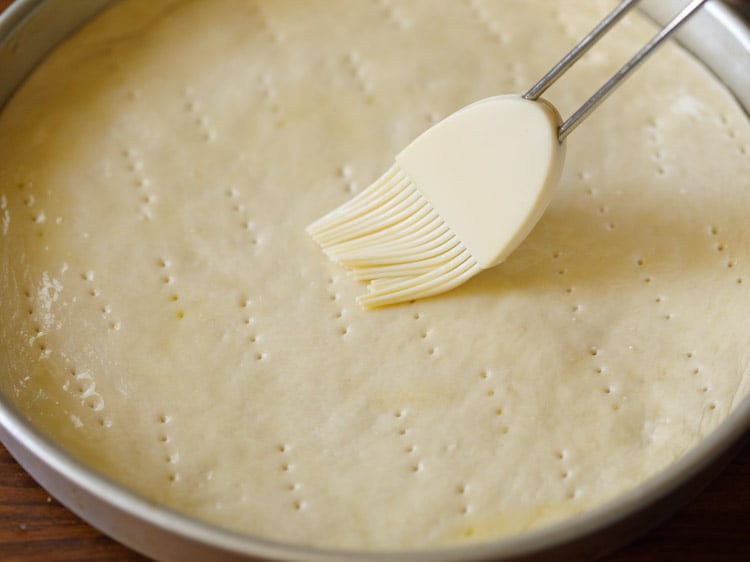 pizza dough being brushed with olive oil with a white silicon pastry brush