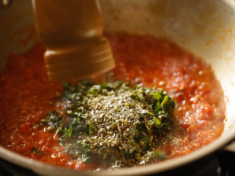 black pepper being crushed with a hand-mill on top of the pizza sauce