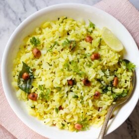 poha or pohe in a white bowl with a lemon wedge and spoon.