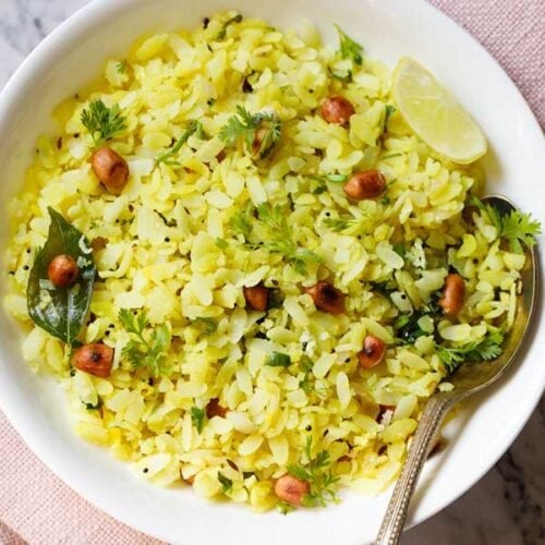 kanda poha or pohe in a white bowl with a lemon wedge and spoon.