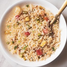 pulao served in a white shallow bowl with a brass serving spoon in the pulao
