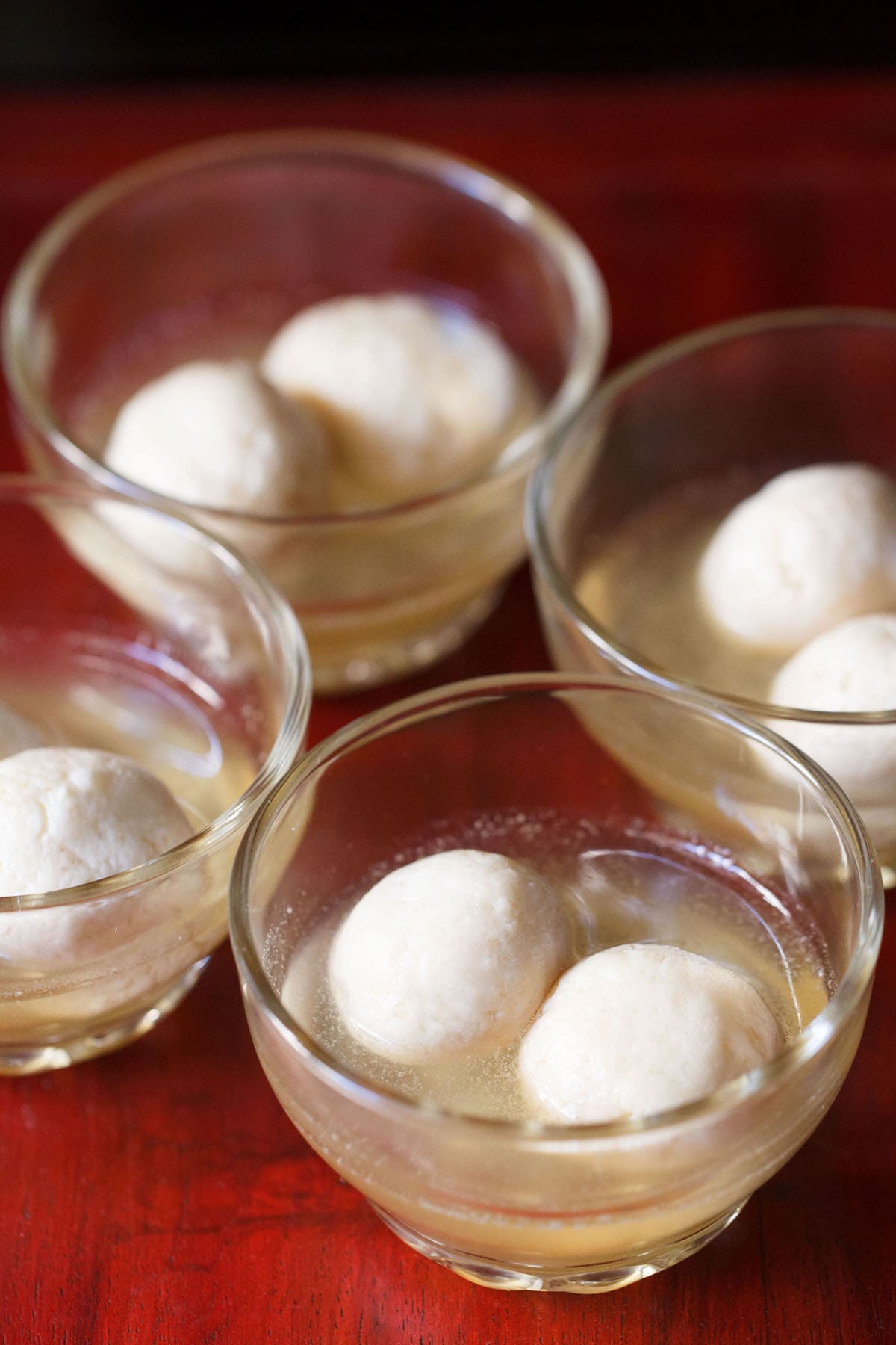 4 small glass bowls with two rasgulla in sugar syrup each