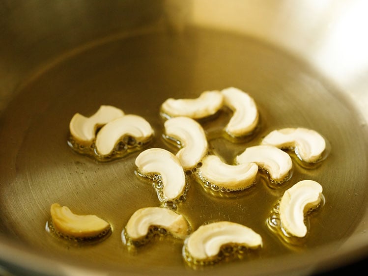 halved cashews added in ghee in pan for making suji ki idli. 