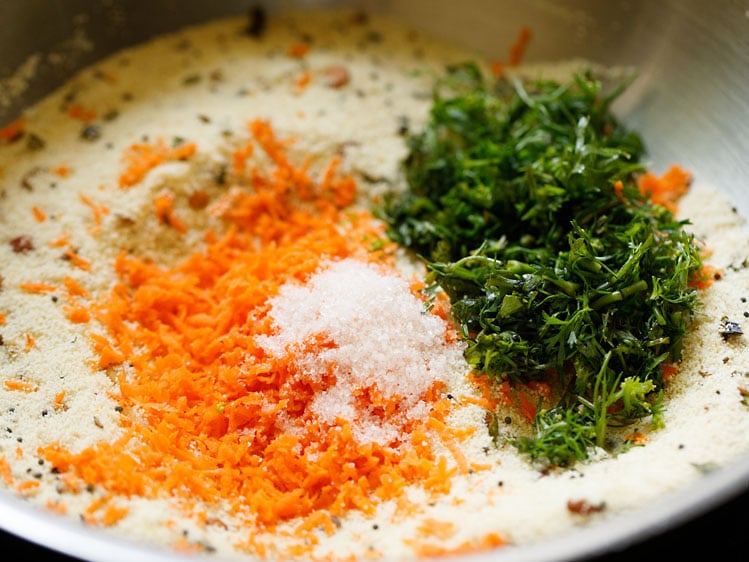 finely grated carrots, chopped coriander leaves and salt added to rava in pan for making suji ki idli. 