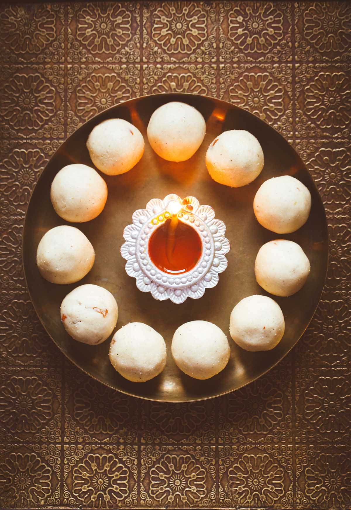 rava laddu in a circle with lit earthern lamp in center on a bronze plate.