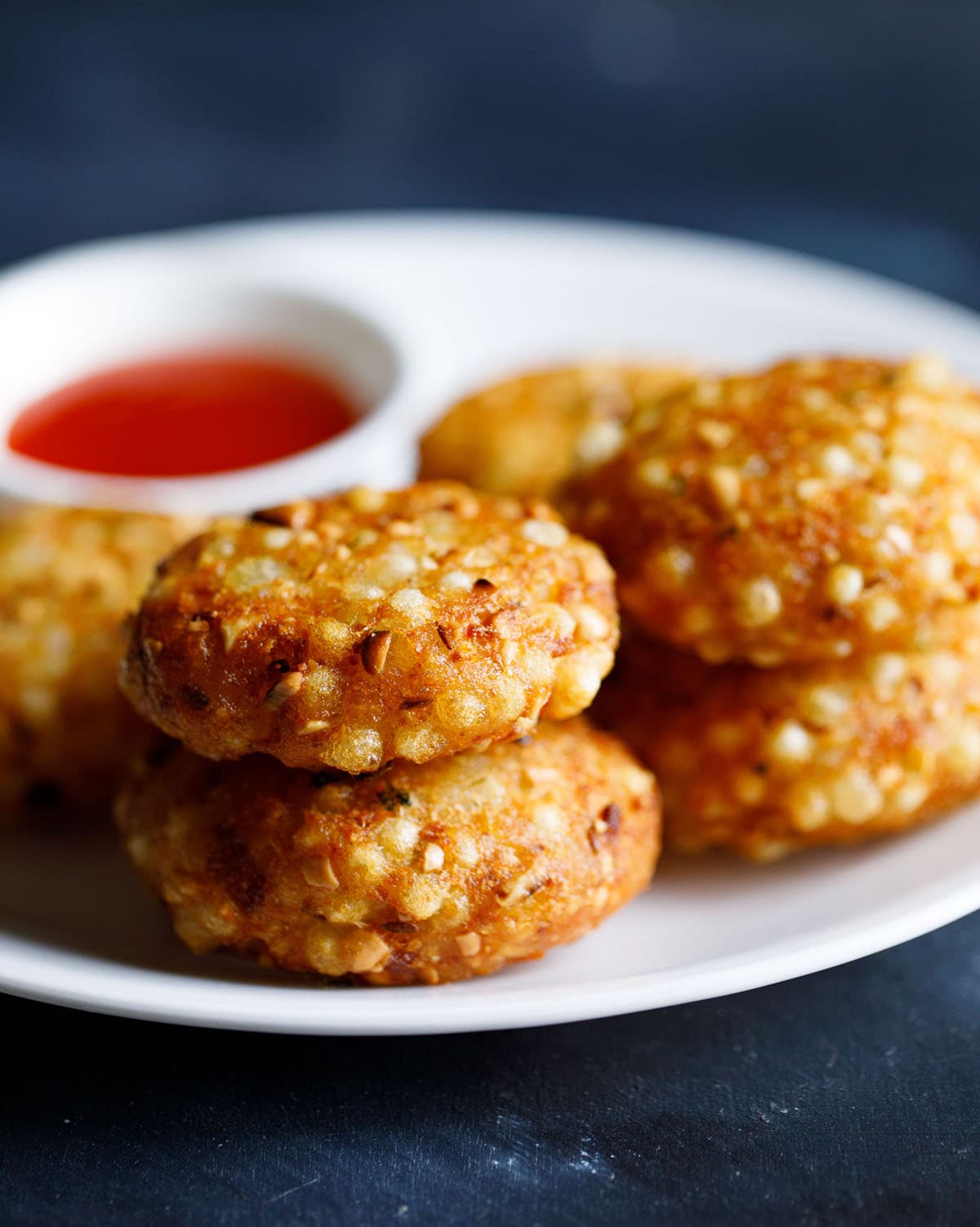 closeup shot of stacks of sabudana vada in a white plate with red chilli sauce in a white bowl