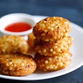 closeup shot of a stack of sabudana vada on top of each other in a white plate with red chilli sauce in a white bowl