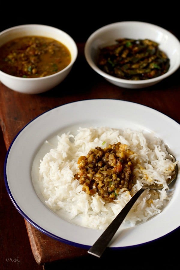 green gram dal on a bed of steamed rice with a spoon in a white plate.