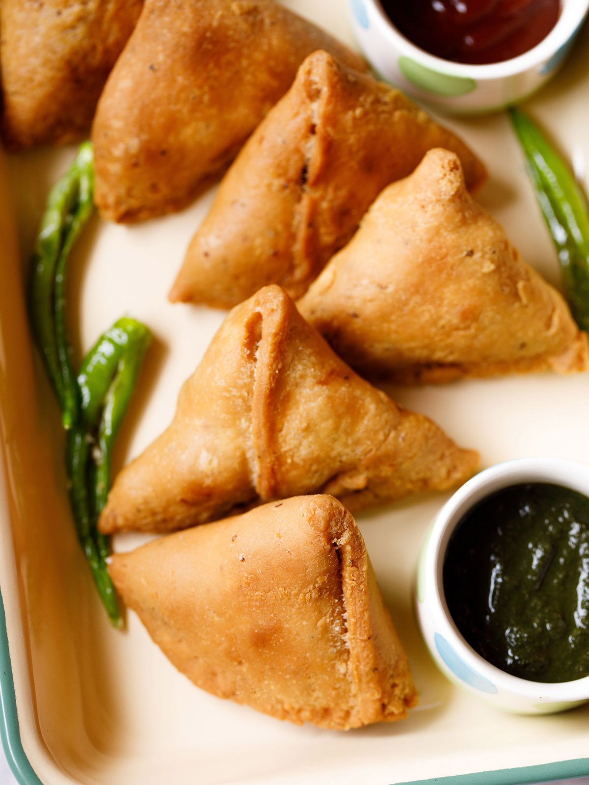 samosa kept in a tray with a bowl of green chutney and some salted fried green chillies