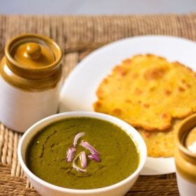 sarson ka saag in a white bowl topped with chopped onions and served with a piece of makki ki roti.