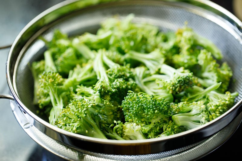 broccoli florets being drained in a steel colander