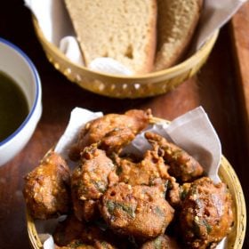 palak pakoda served in a bowl with a side of wheat bread slices and coriander chutney on a wooden board.