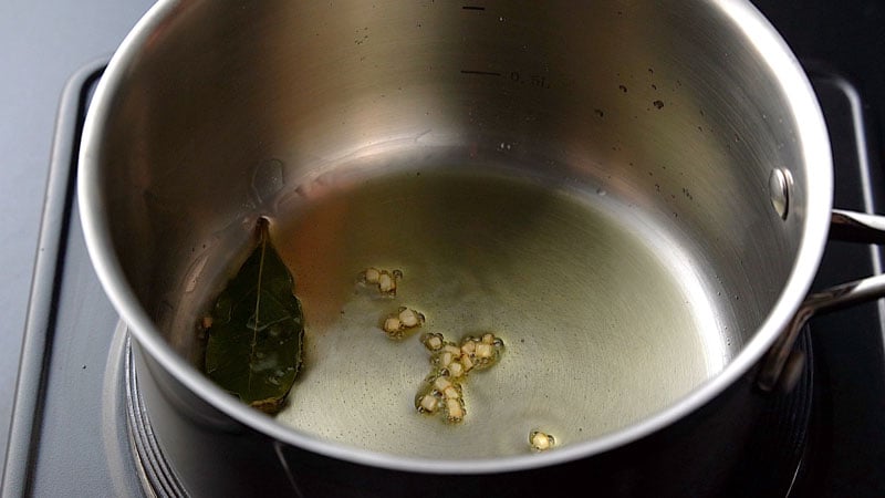 adding garlic to the bay leaf in a saucepan