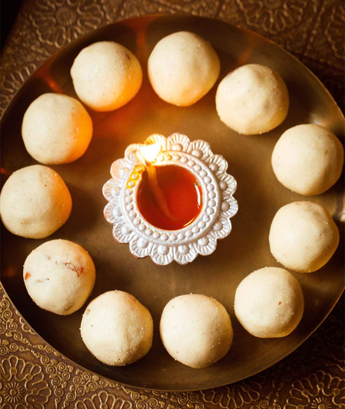 rava ladoo in a circle with lit earthen lamp in center on a bronze plate.