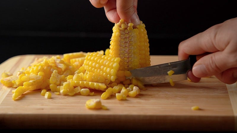 corn cobs being sliced to remove sweet corn kernels