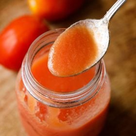 tomato puree in a spoon on top of a glass jar filled with tomato puree and two tomatoes placed on top left side