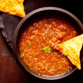 salsa served in a black wooden bowl with a nacho chip dipped in the salsa