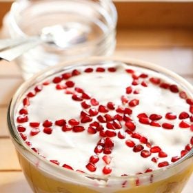 top shot of trifle with top cream layer garnished with wheel like design with pomegranate seeds.