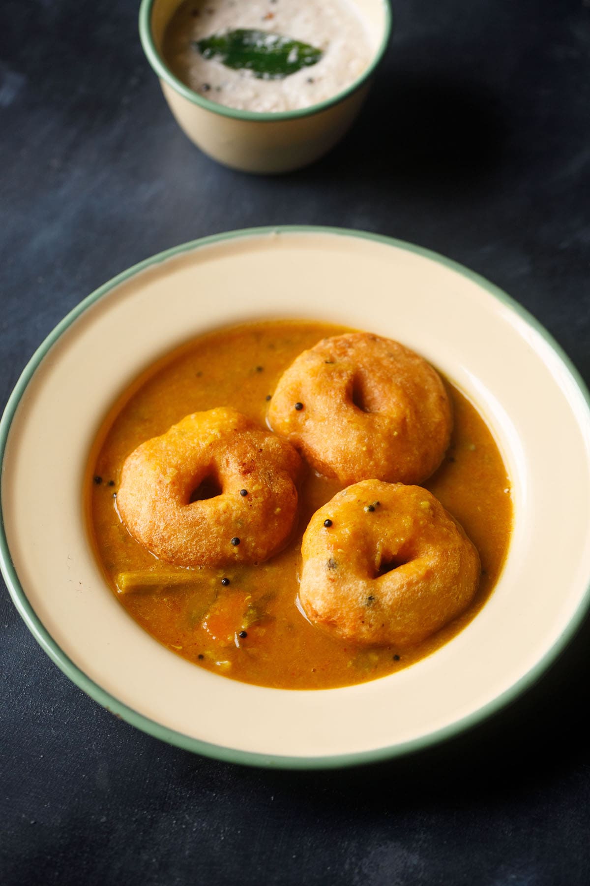 vada sambar in a beige colored shallow plate with medu vada placed on sambar