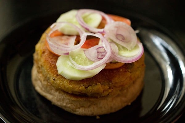 veggie patty topped with slices of onions, cucumber and tomatoes