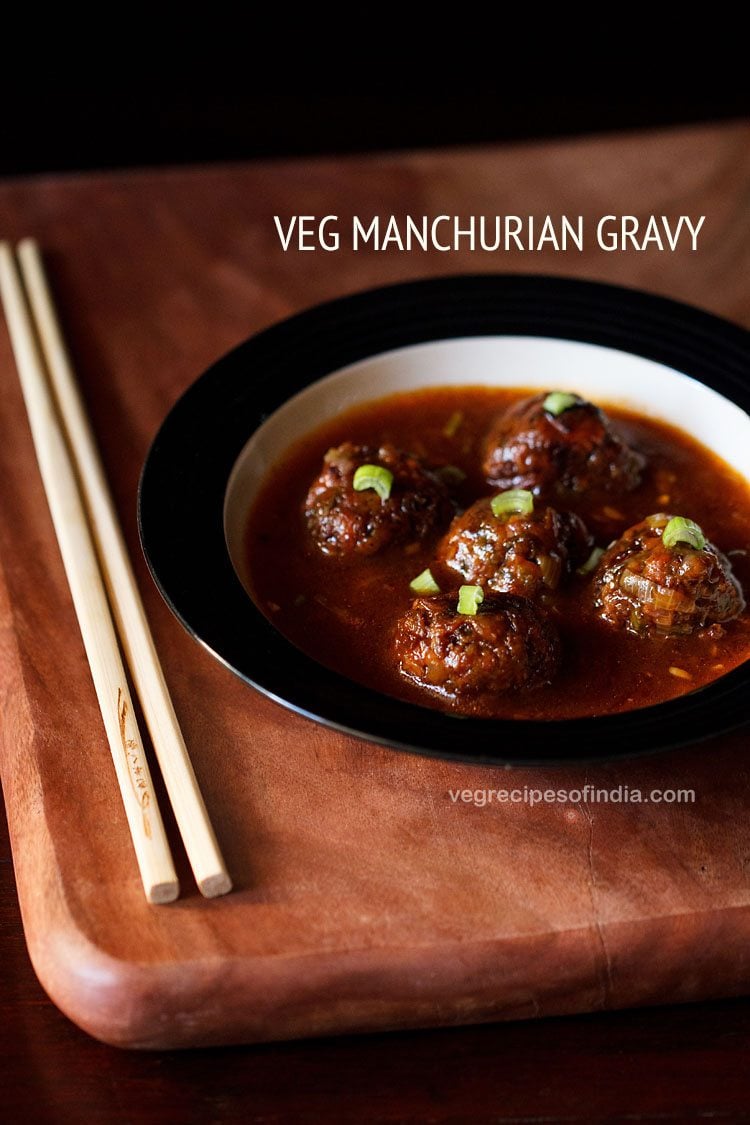 veg manchurian gravy garnished with chopped spring onion greens and served in a black rimmed bowl with chopsticks kept on the left side and text layover.