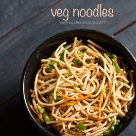 veg noodles served in a black bowl on a dark blue-gray wooden board