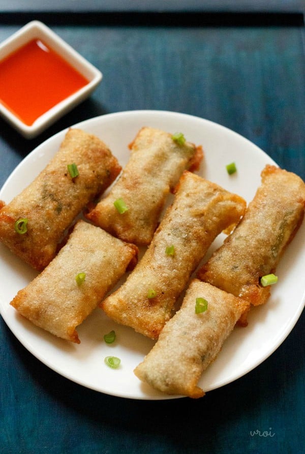 white serving plate with 6 crispy fried veggie spring rolls garnished with green onions