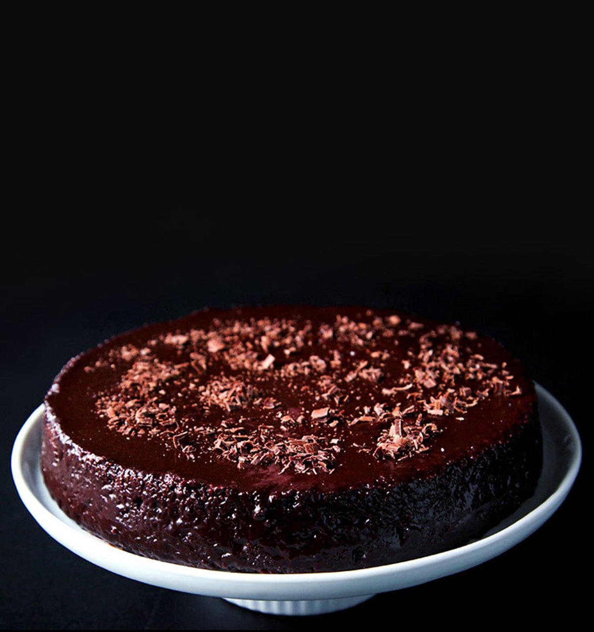 vegan eggless chocolate cake on a white cake stand on a black board