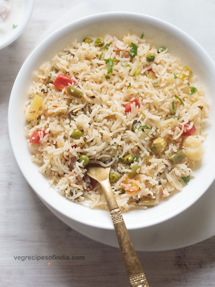 vegetable pulao served in a white shallow bowl with a brass spoon in the pulao.