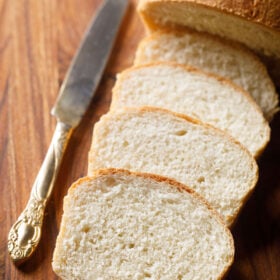 white bread loaf sliced with the slices placed on top of each other with an antique butter knife on a brown wooden board